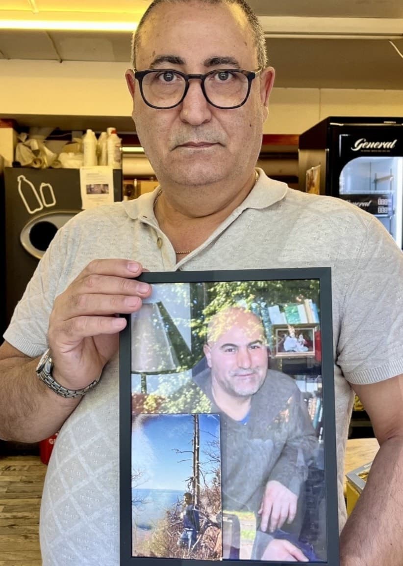 Ali Kamrani står inne på Göta All-Livs i Borås och håller upp en inramad bild av sin bror Oktay. Bakom honom syns butikens kylskåp och hyllor fyllda med olika varor.
