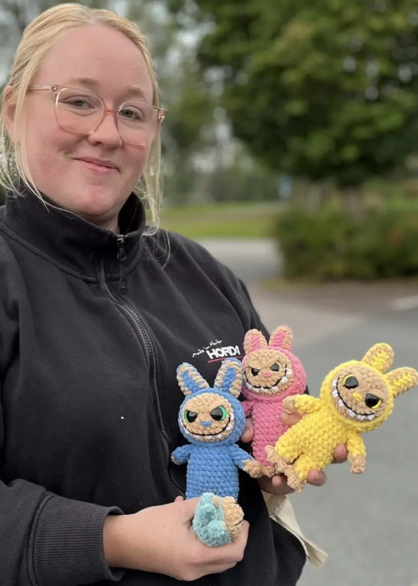 Emma Petersson från Horda utanför Värnamo visar upp tre färgglada, egenvirkade monsterdockor utomhus på en parkeringsplats.